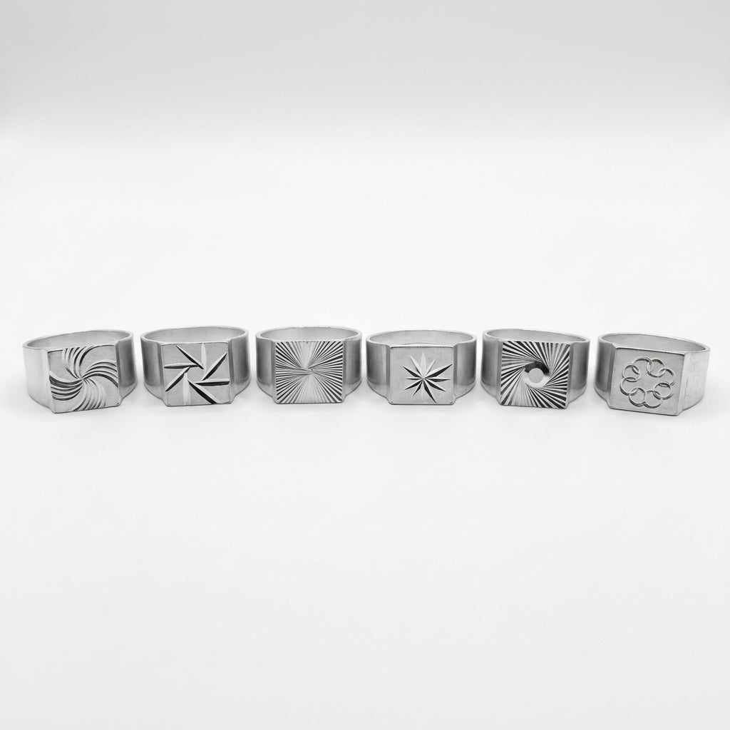 Le Tirage : les 6 chevalières gravées en aluminium alignées, chacune avec un motif différent