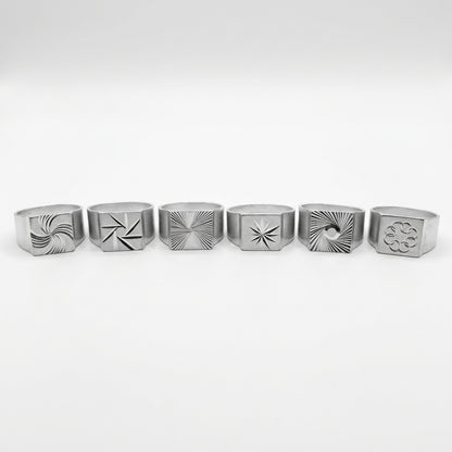 Le Tirage : les 6 chevalières gravées en aluminium alignées, chacune avec un motif différent